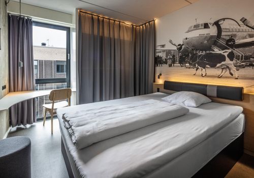 Uniform hotel room with fitted bed, wall panel and a compact bathroom door